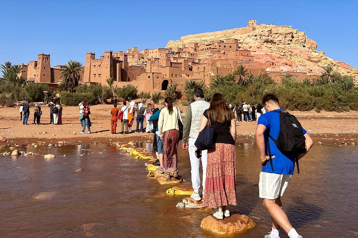 Viajeros cruzando el río sobre piedras bajo Aït Ben Haddou