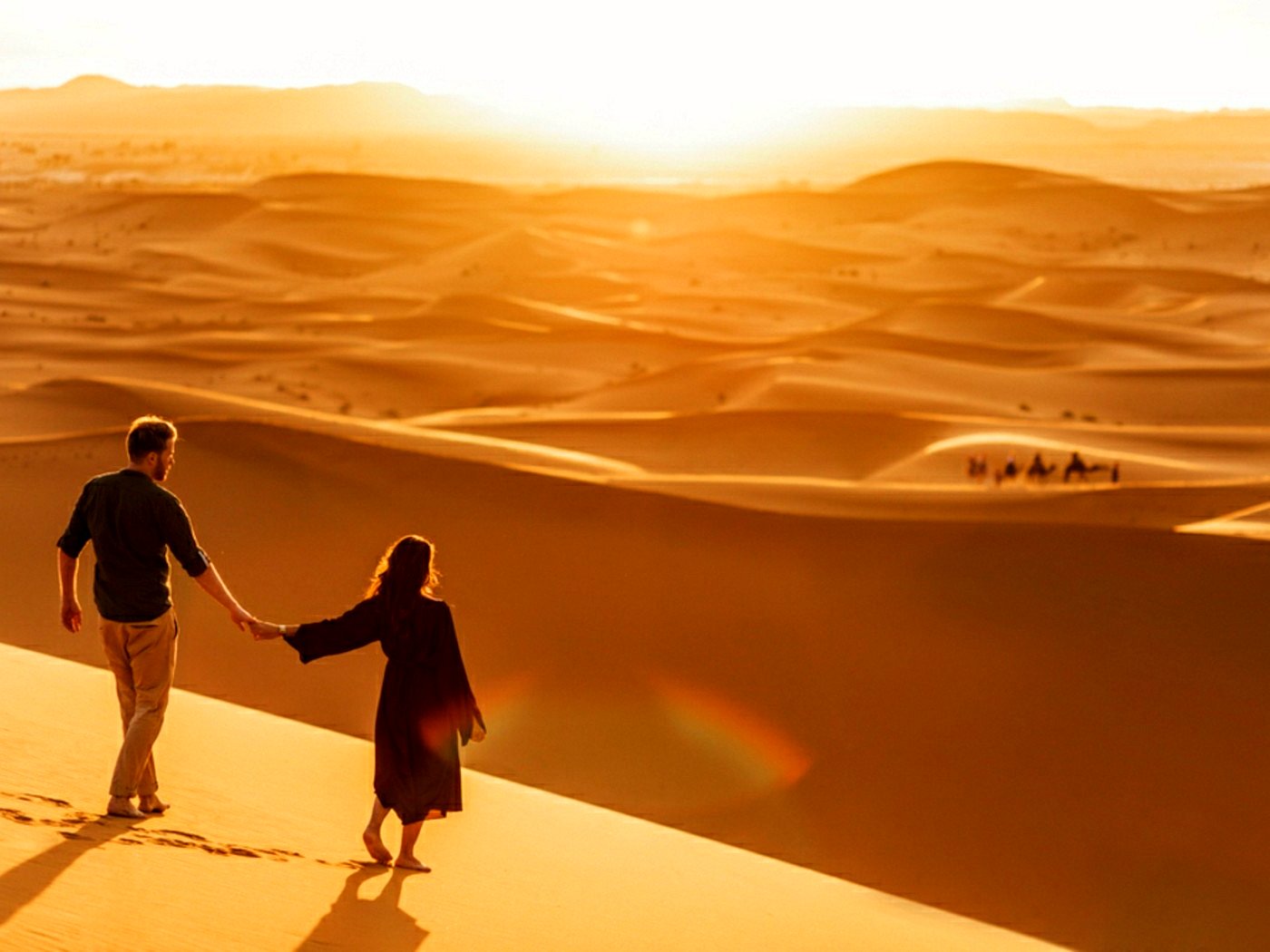 Reizigers lopen bij zonsondergang over Sahara-duinen